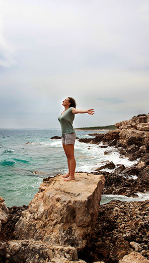 Jeune femme levant les bras au ciel en regardant l'océan